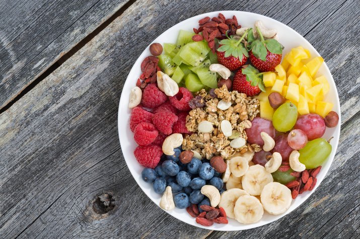 Mixed fruit, nuts and granola in a white bowl on wood table