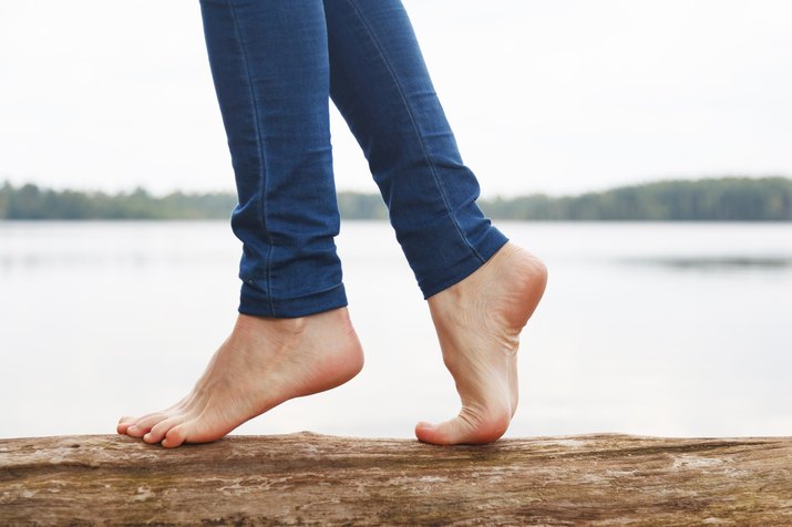 A woman's bare feet walking on a log near a lake