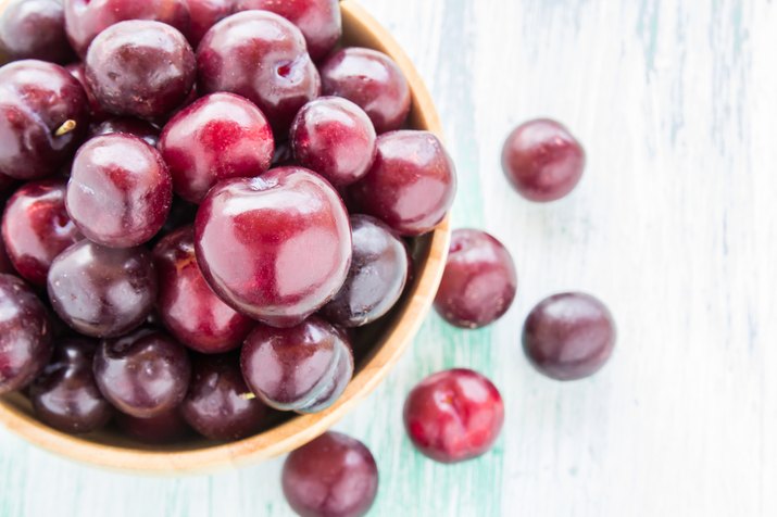 red Cherries in wooden bowl on wooden table background