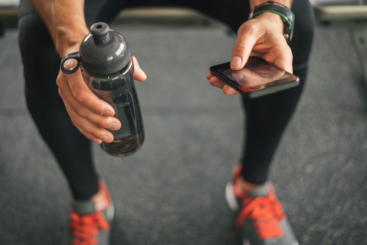 Fitness man looking to the phone for motivation before workout