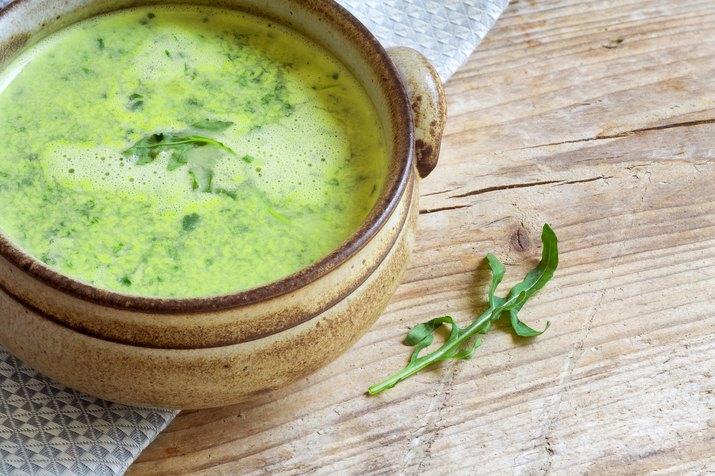 green vegetable soup in a brown bowl on rustic wood