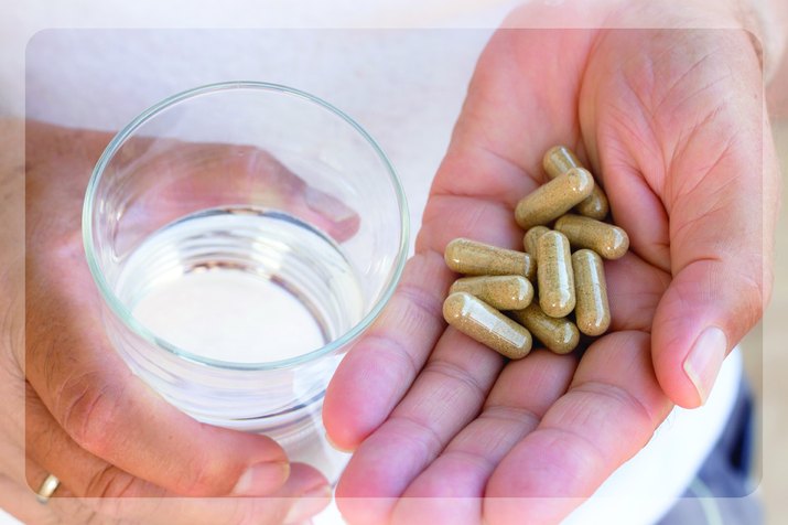 Hand holding vitamins and supplements next to a glass of water