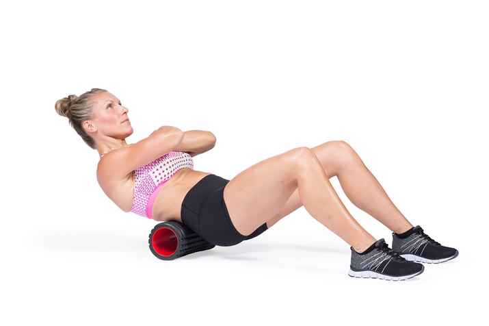Athlete massaging upper back muscles with foam roller.