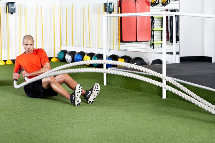 Man doing seated hip-toss rotations with the battle ropes