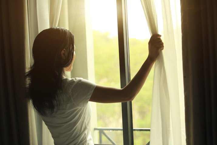 Woman opening curtains to wake up before exercise.