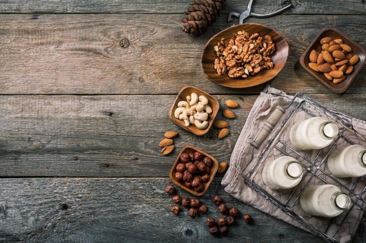 Vegan milk from nuts in glass bottles with various nuts on old wooden background, top view with copy space