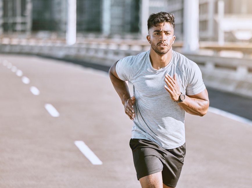 young adult wearing a gray T-shirt and black shorts running on a track outside as an example of a negative feedback loop during exercise