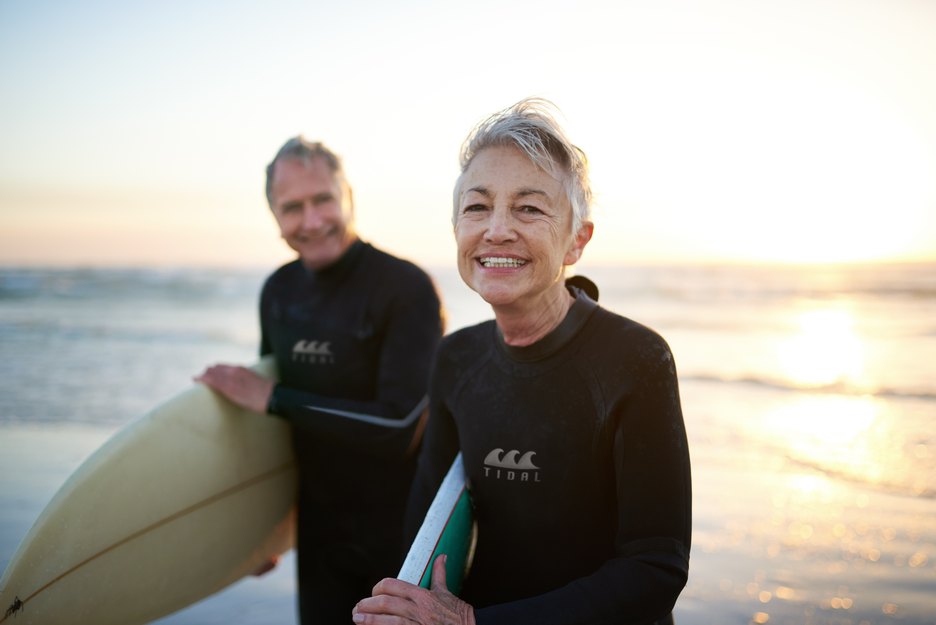 an older couple at the ocean holding surfboards and smiling