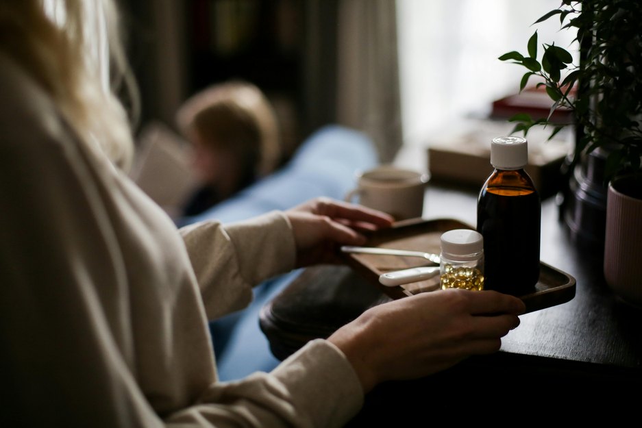 a close up of an adult caregiver bringing a small wooden tray of cold medicines to a sick child in the background