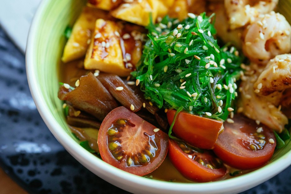 a close up of a bowl of stir-fry with tofu, tomatoes and seaweed salad